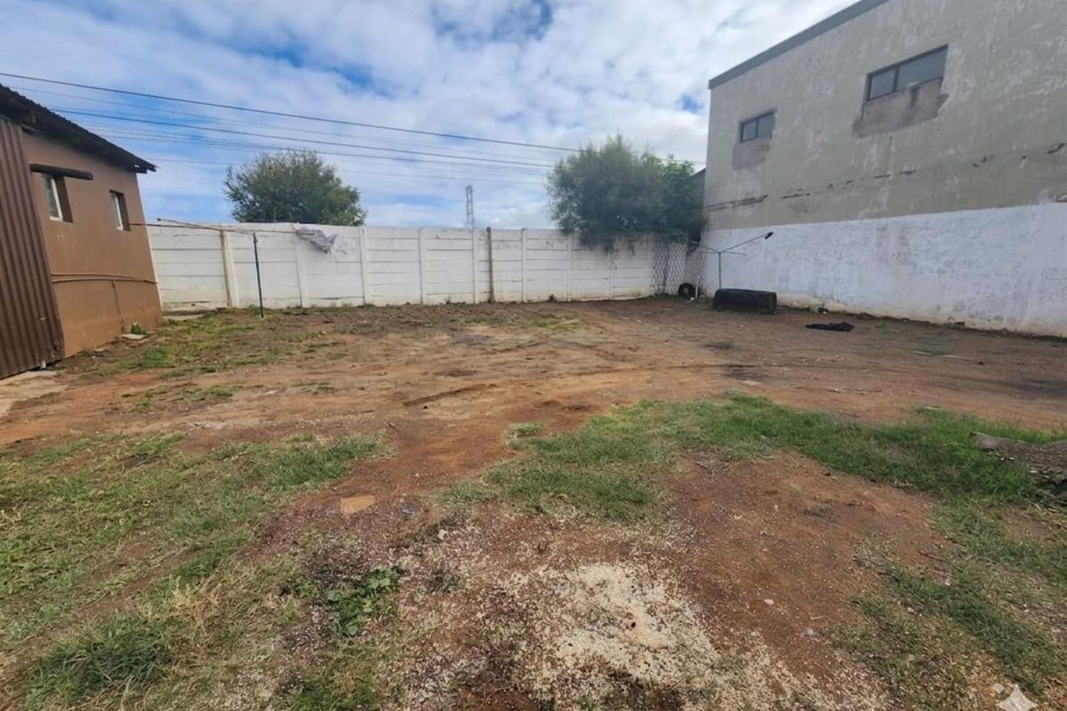 A large, undeveloped rear yard area featuring a perimeter boundary wall and adjacent building structures, offering significant potential for landscaping or development.