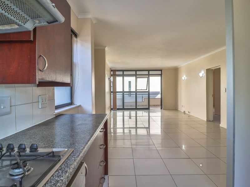 Spacious open-plan living area featuring a functional kitchen with gas hob, granite countertops, and tiled flooring, leading to a balcony with natural light.