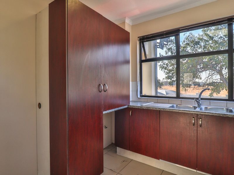 A functional kitchen area featuring dark wood-look cabinetry, laminate countertops, a stainless steel sink, and tiled flooring with a window view.