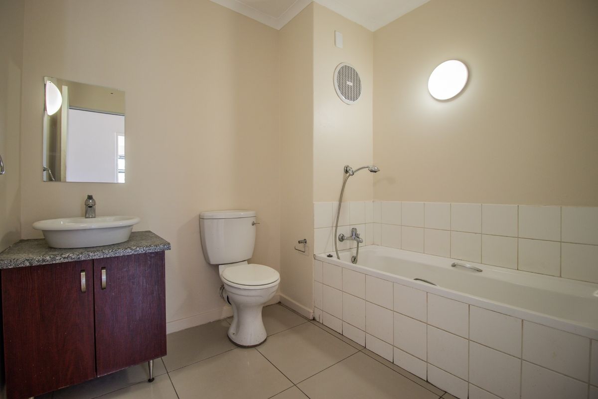 A functional bathroom featuring a tiled bathtub with handheld shower, a vanity with vessel sink, and a wall-mounted extractor fan.
