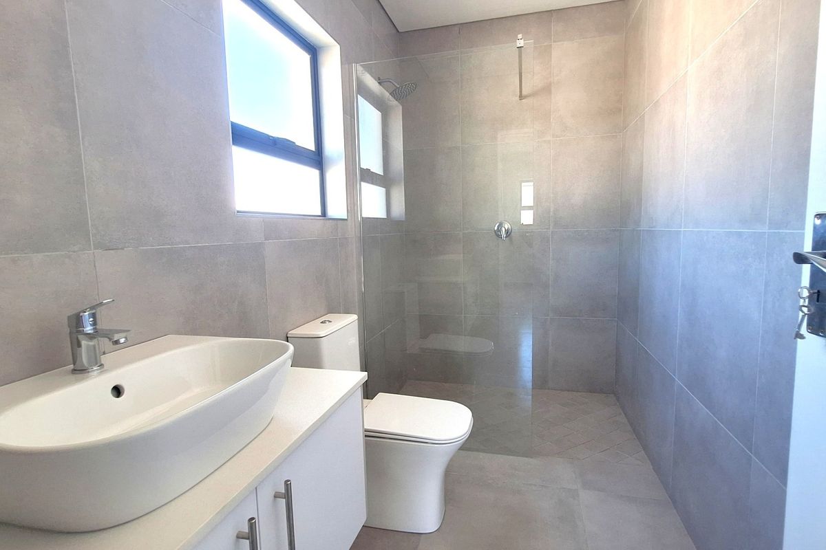 Modern bathroom featuring large format grey wall tiles, a glass walk-in shower, a contemporary vessel sink vanity, and a back-to-wall toilet.