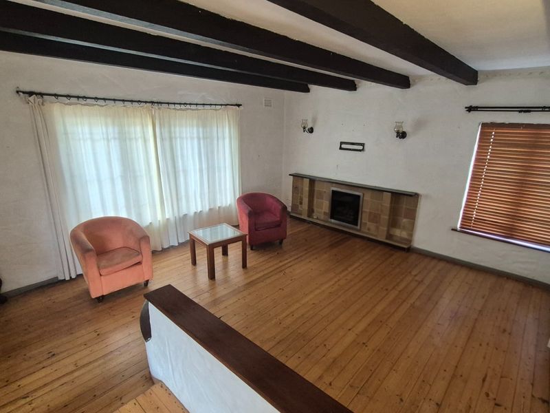 Spacious living room featuring exposed timber ceiling beams, polished wooden flooring, and a built-in fireplace with a tiled hearth.