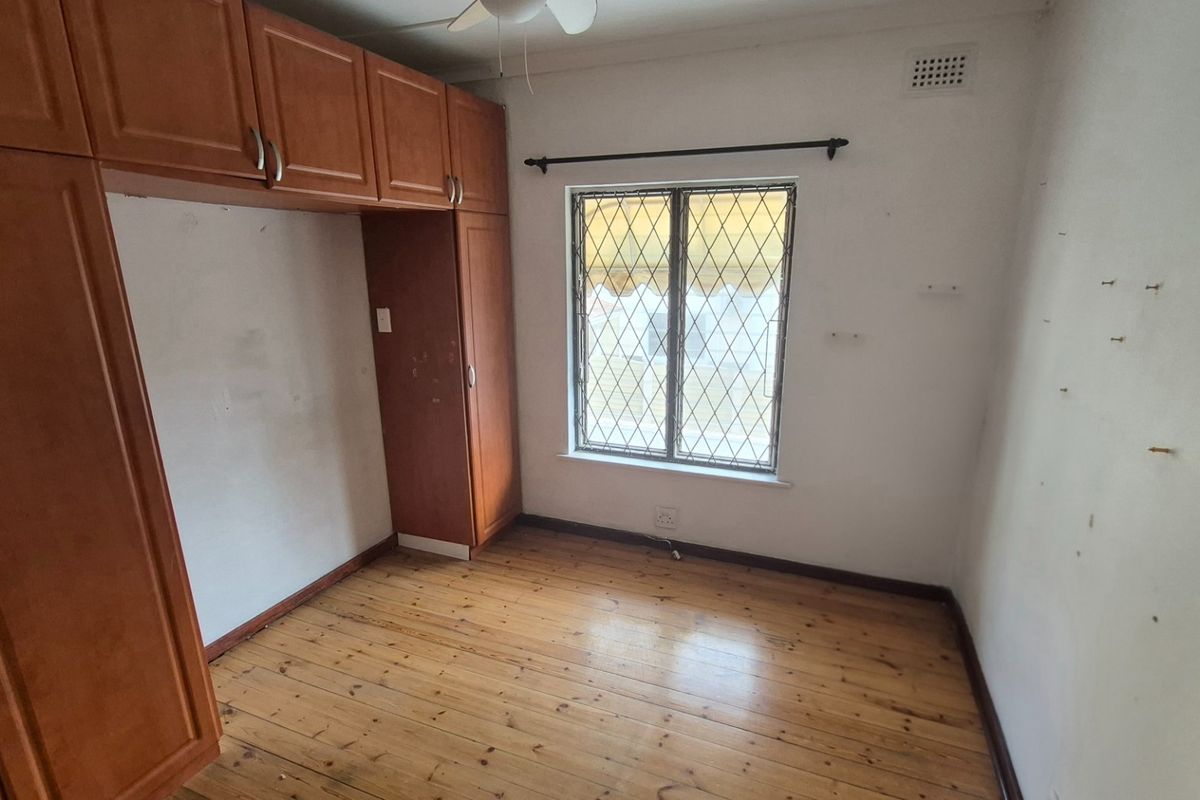 A bedroom featuring built-in wooden cabinetry, timber flooring, and a security-grilled window, requiring cosmetic updates to refresh the space.