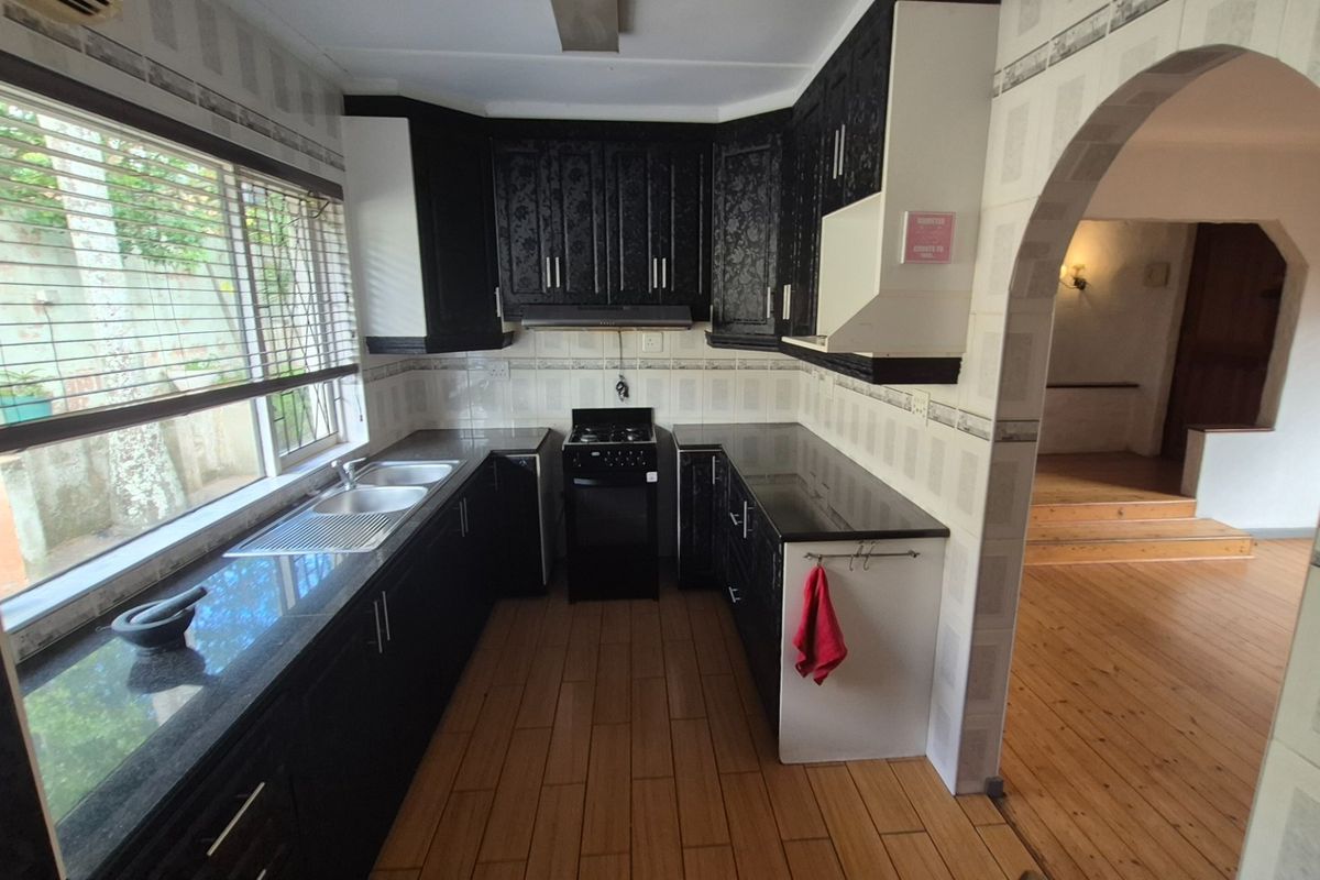A functional kitchen featuring dark cabinetry, granite countertops, a built-in stove, and tiled flooring, with an arched entryway leading to the adjacent living area.
