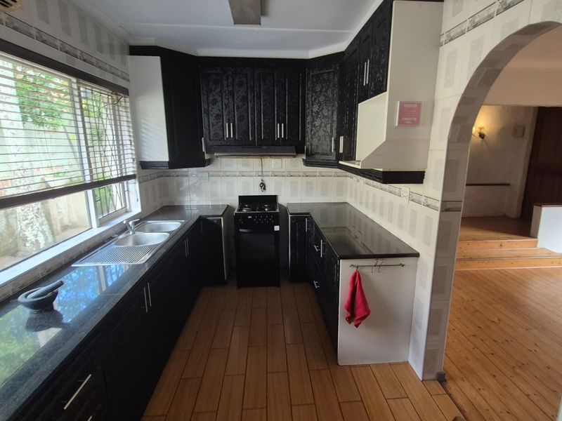 A functional kitchen featuring dark cabinetry, granite countertops, a built-in stove, and tiled flooring, with an arched entryway leading to the adjacent living area.