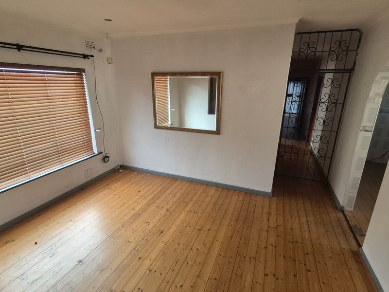 A vacant living room featuring polished timber flooring, wooden venetian blinds, and a decorative security gate leading to the hallway.