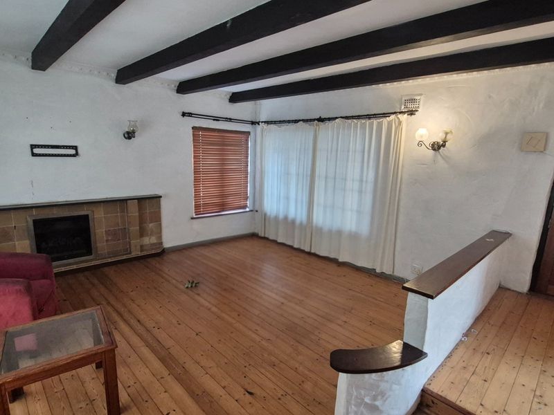 Spacious living room featuring exposed timber ceiling beams, polished wooden flooring, and a built-in fireplace with a tiled hearth.