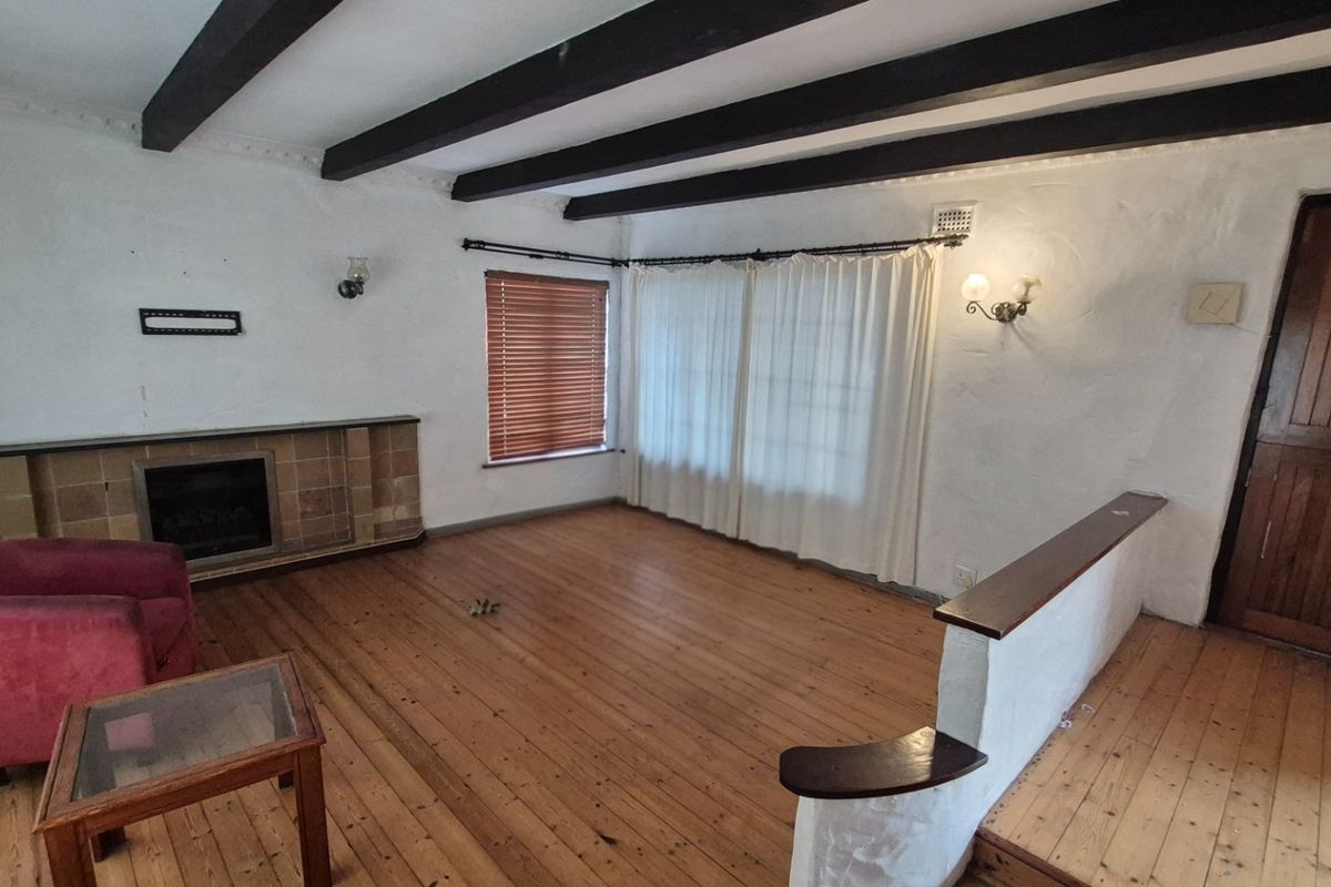 Spacious living room featuring exposed timber ceiling beams, polished wooden flooring, and a built-in fireplace with a tiled hearth.