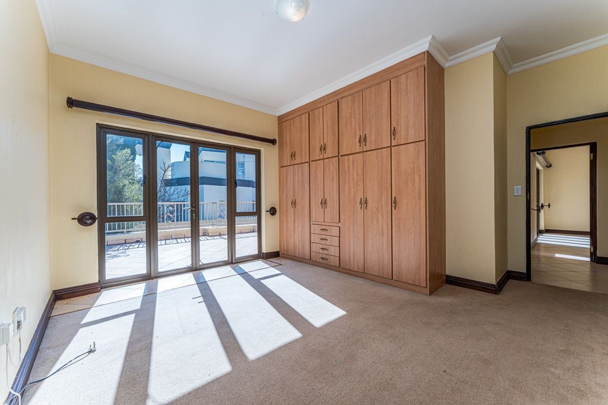 Spacious bedroom featuring built-in wooden cabinetry, neutral wall finishes, and large glass sliding doors providing direct access to an outdoor balcony area.
