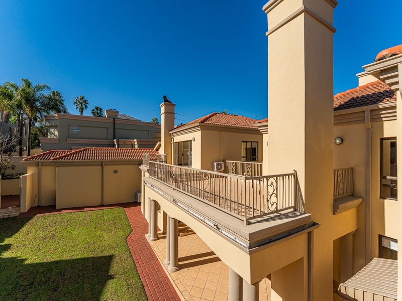 A well-maintained rear exterior view featuring a spacious balcony, covered patio area, terracotta roof tiles, and a landscaped garden with paved pathways.