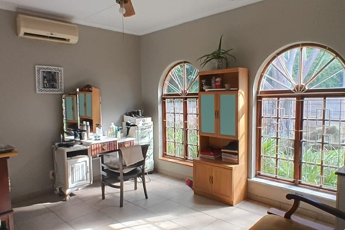 A bedroom or multi-purpose room featuring arched windows with security bars, tiled flooring, and a wall-mounted air conditioning unit.