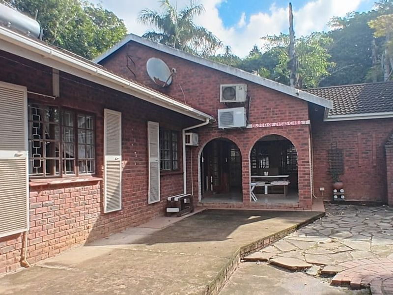 Rear exterior view featuring a brick facade, covered patio area, built-in outdoor braai, and paved courtyard space.
