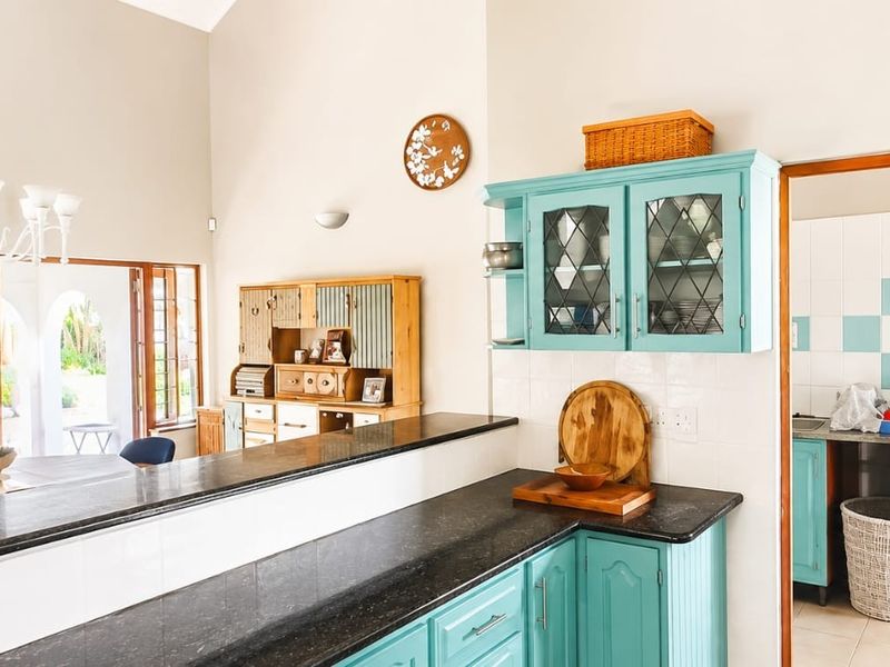 Open-plan kitchen area featuring vibrant teal cabinetry, dark stone countertops, and a vaulted ceiling, seamlessly connecting to the dining space and scullery.