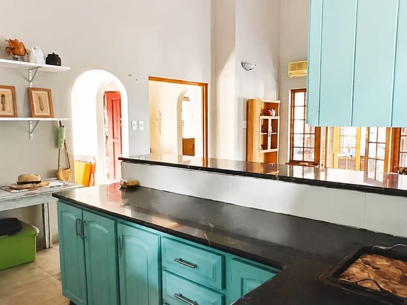 Kitchen featuring teal cabinetry, dark stone countertops, and an open-plan layout with arched doorways leading to adjacent living spaces.