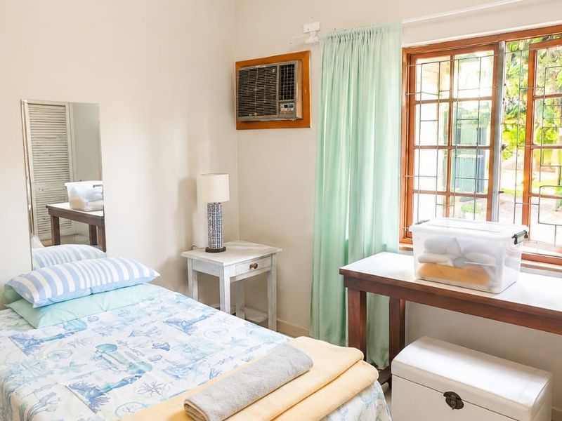A functional bedroom featuring a window air conditioning unit, security bars on the window, and a wooden door.