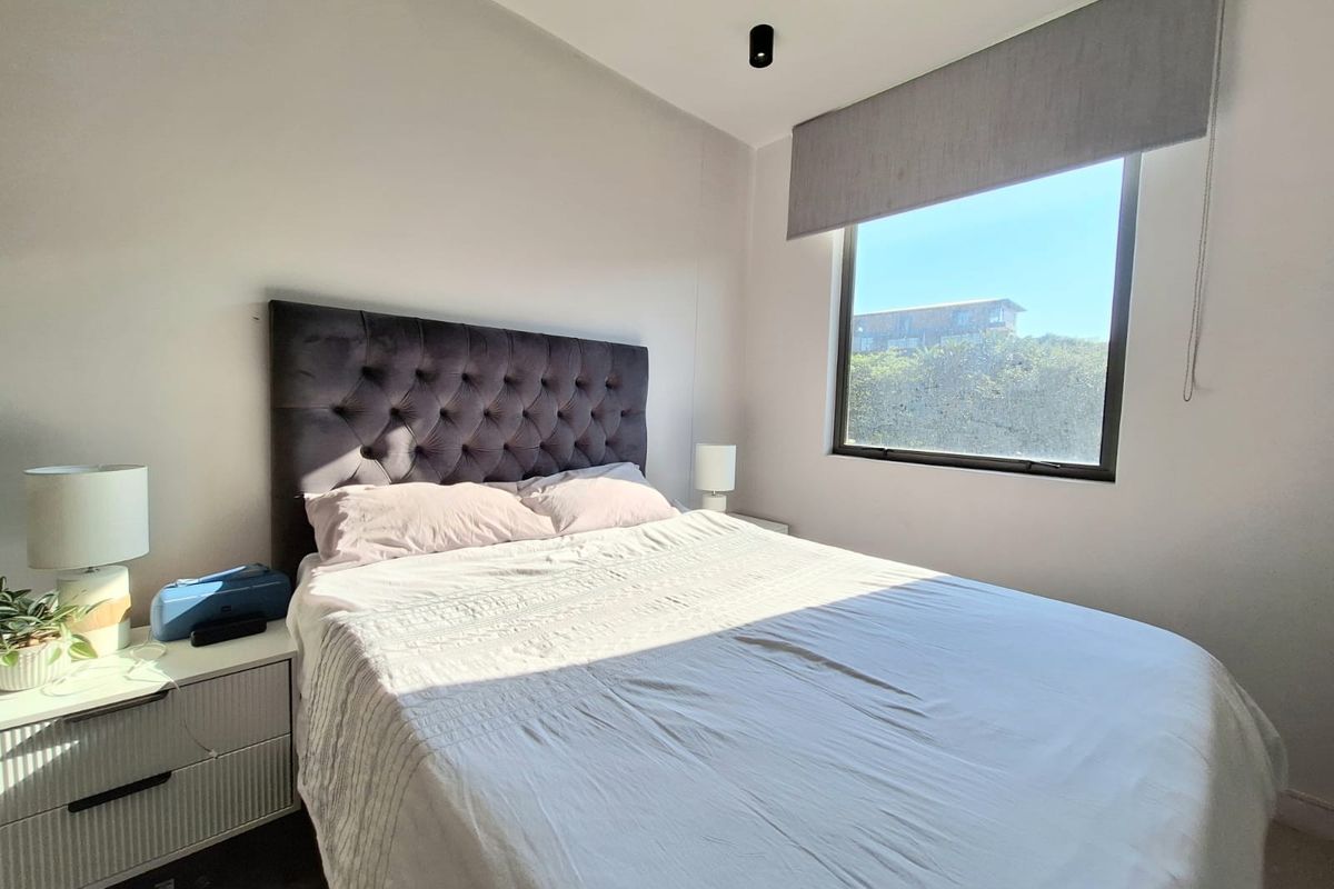 A bright and modern bedroom featuring a large window with a roller blind and contemporary ceiling lighting.