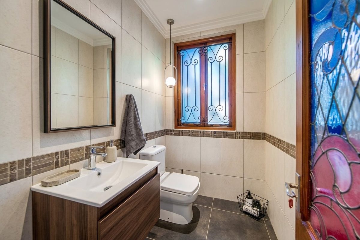 A well-maintained bathroom featuring a modern vanity, dual-flush toilet, tiled finishes, and a window with decorative security grille.