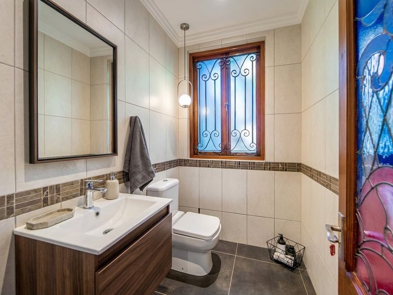 A well-maintained bathroom featuring a modern vanity, dual-flush toilet, tiled finishes, and a window with decorative security grille.