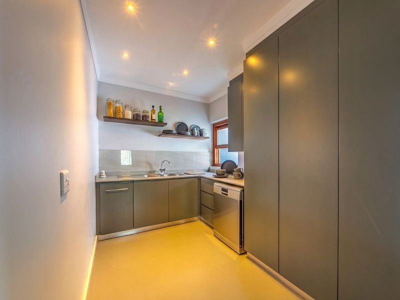 A modern, compact scullery featuring sleek grey cabinetry, stainless steel sink, integrated dishwasher, and floating shelving for efficient storage and prep space.