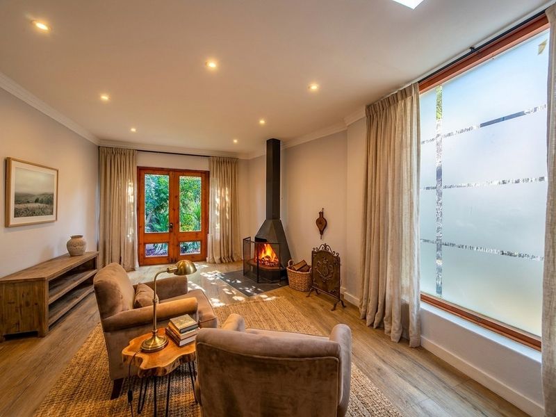 A cozy living room featuring a modern freestanding fireplace, timber-framed glass doors leading to the garden, and warm laminate flooring with recessed lighting.