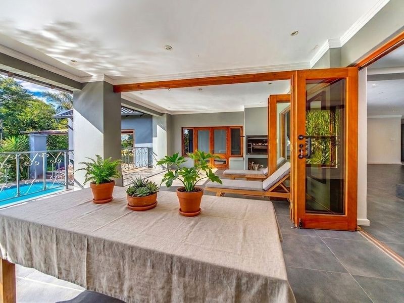 Spacious covered patio featuring tiled flooring, built-in braai, and wooden folding doors, offering seamless indoor-outdoor flow overlooking the swimming pool.