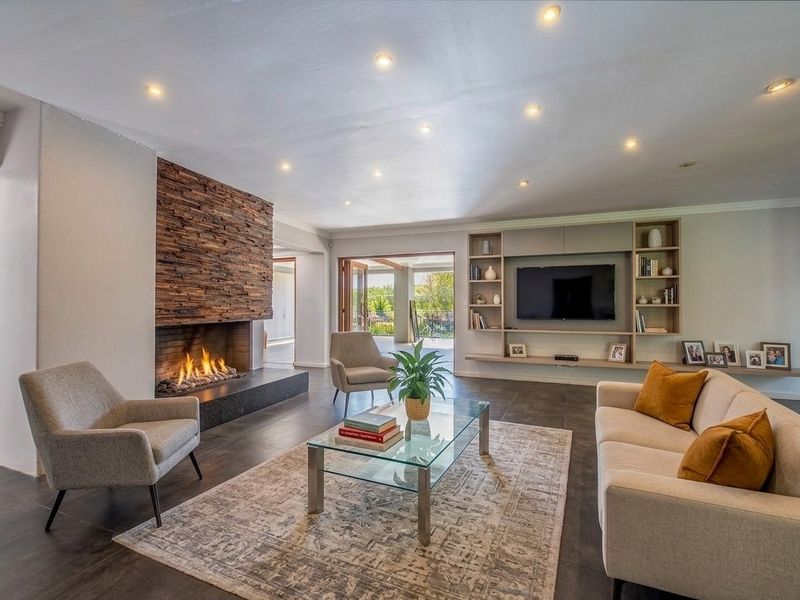 Spacious living room featuring a striking stone-clad fireplace, custom built-in shelving, modern tiled flooring, and seamless access to the outdoor patio area.