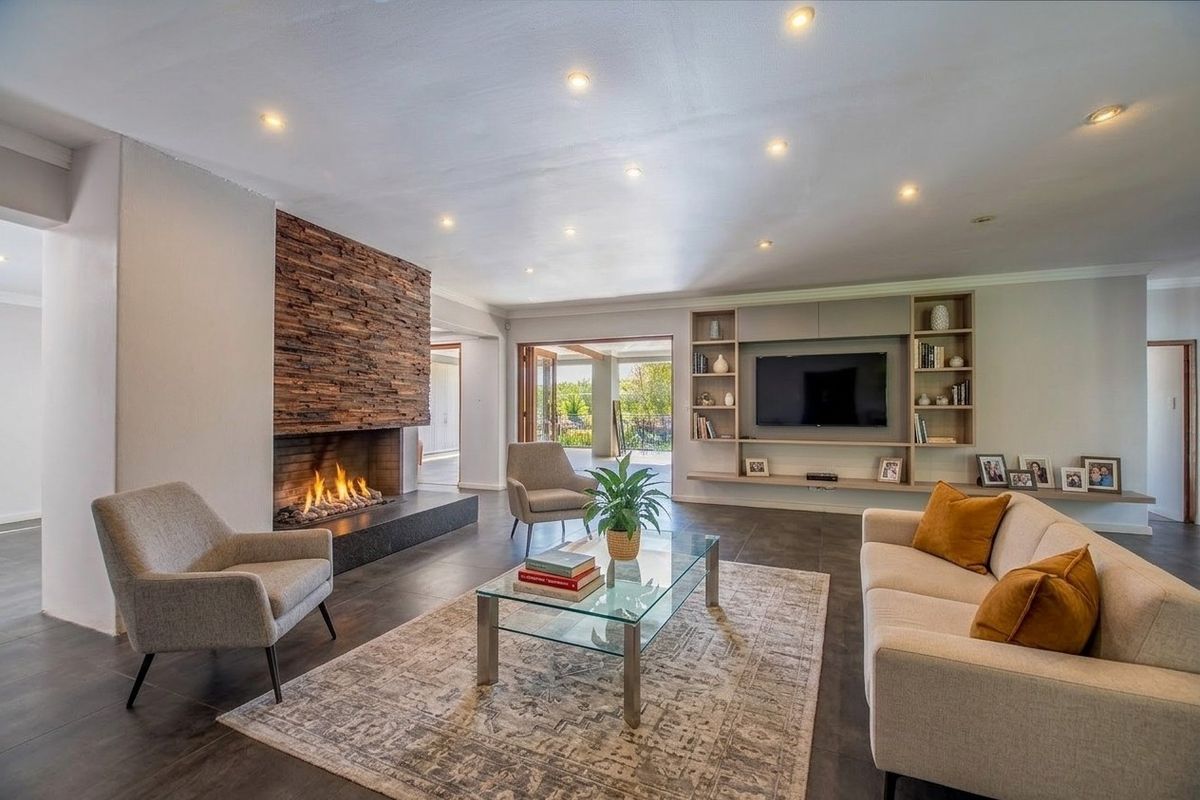 Spacious living room featuring a striking stone-clad fireplace, custom built-in shelving, modern tiled flooring, and seamless access to the outdoor patio area.