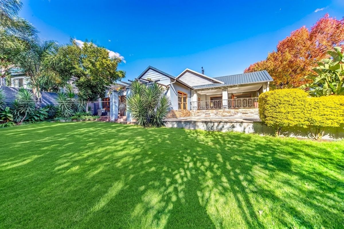 Rear view of the house featuring a spacious lawn, landscaped garden, and a covered patio area with stone accents and metal roofing.
