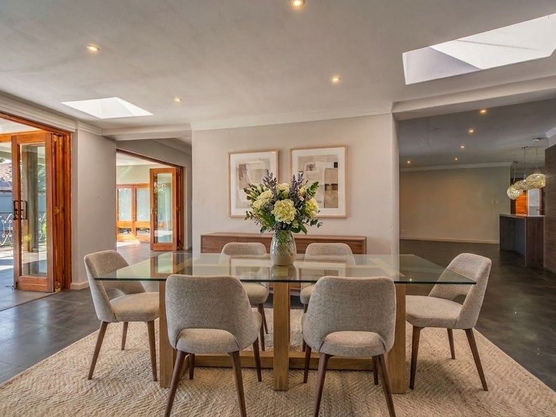 Spacious dining area featuring tiled flooring, recessed lighting, and dual skylights, with seamless access to the outdoor patio through timber-framed glass doors.