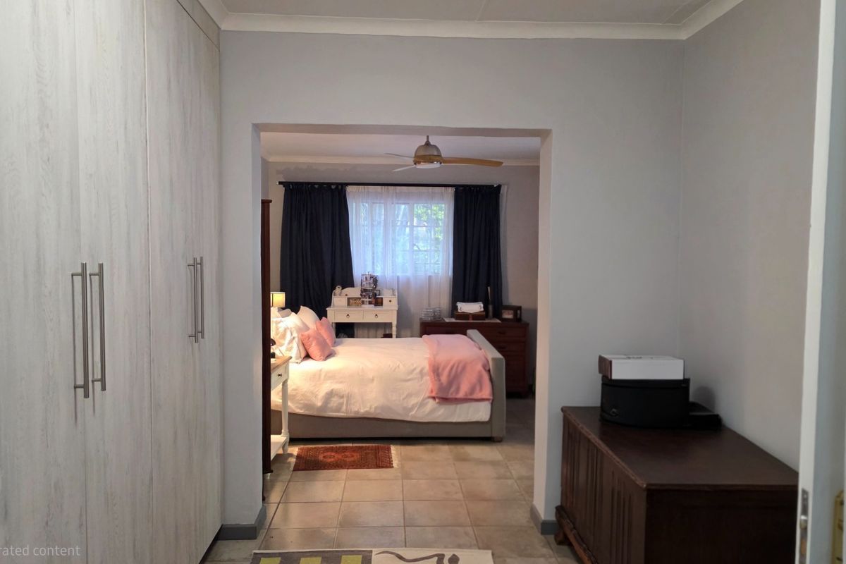 A spacious bedroom featuring built-in wardrobes with light wood-grain finish and tiled flooring, leading into a comfortable sleeping area.