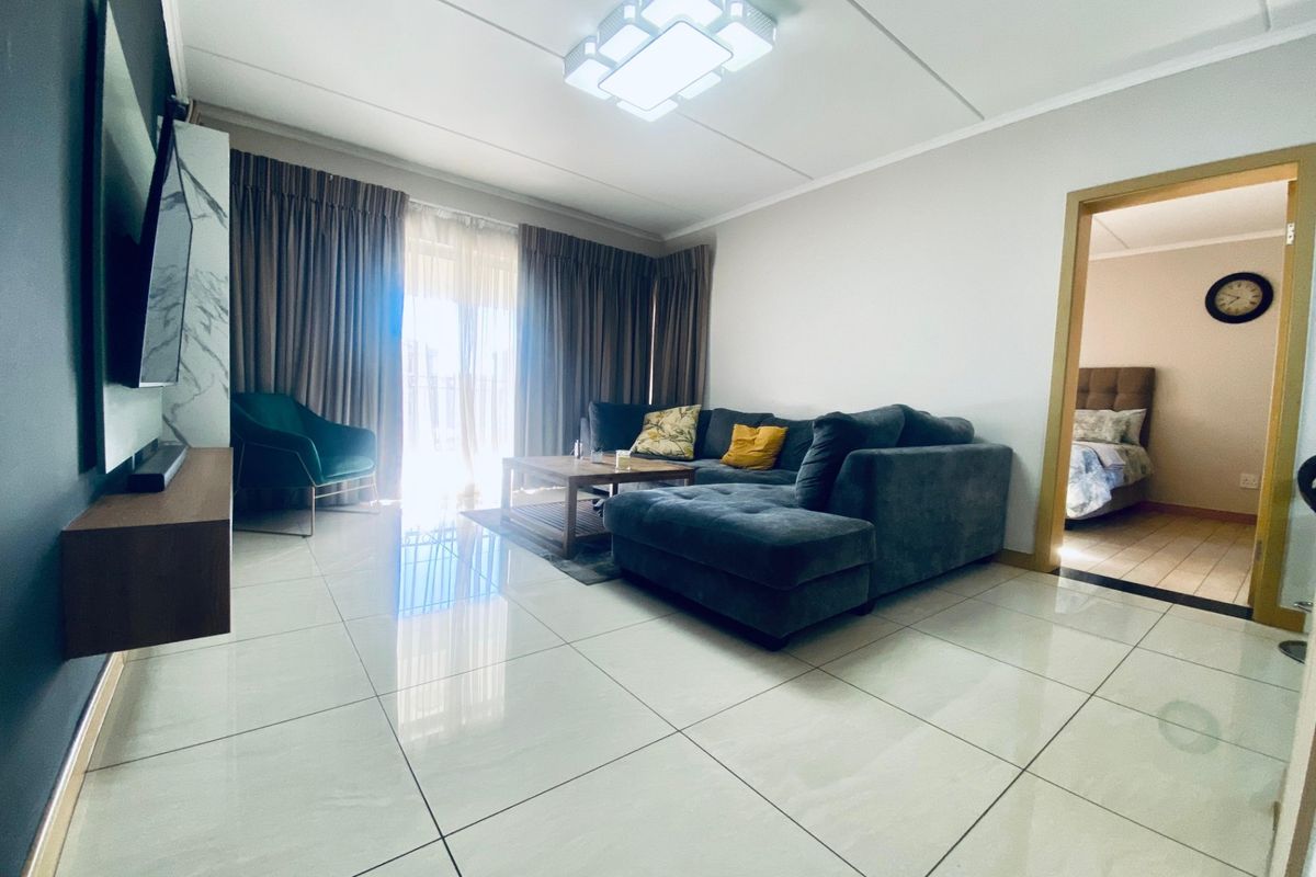 A bright, open-plan living area featuring polished porcelain floor tiles, a modern ceiling light fixture, and direct access to a balcony.