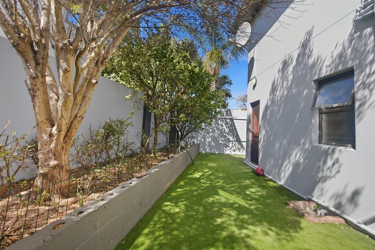 A side garden area featuring artificial turf, a concrete retaining wall, and a secure side entrance to the property.