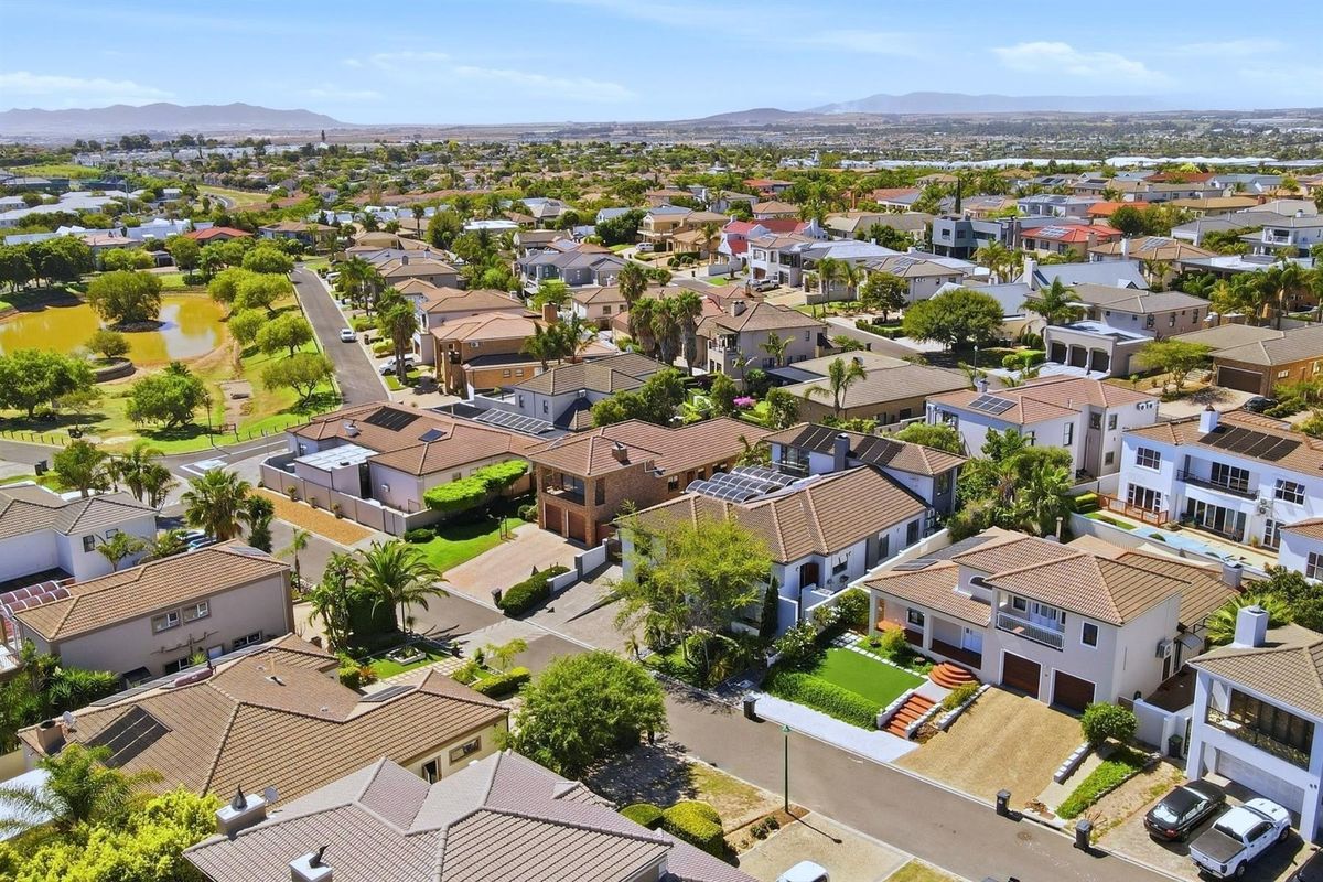 An elevated aerial view of a residential estate featuring multiple homes with tiled roofs, solar panels, and well-maintained suburban landscaping.