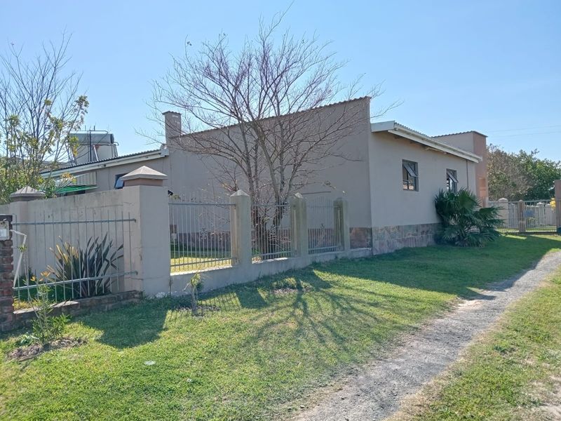 Exterior view of the farm property featuring a perimeter boundary wall with metal fencing, a gravel driveway, and a single-story dwelling structure.