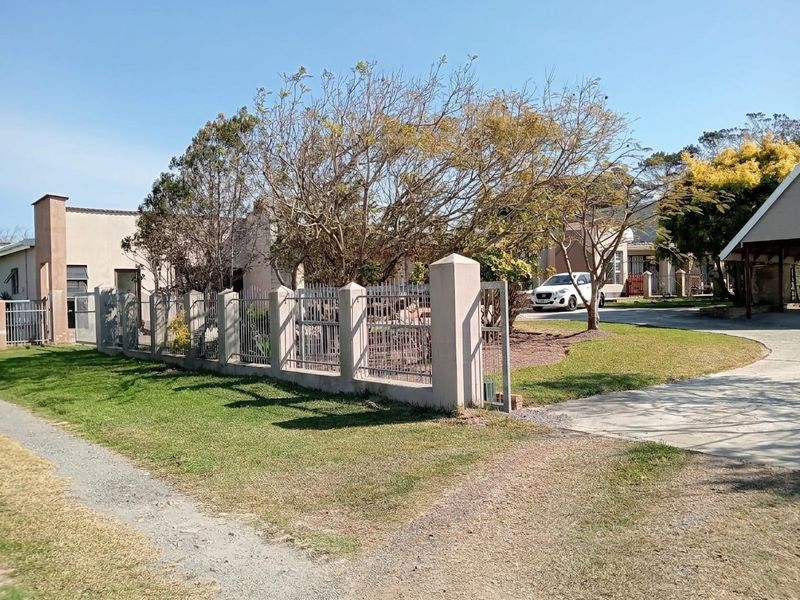 A view of the property entrance featuring a concrete and metal perimeter fence, paved driveway, and established garden area.
