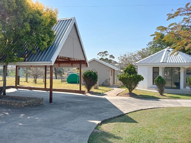 Exterior view of the farm property featuring a covered outdoor structure, paved pathways, and surrounding garden areas with established trees.