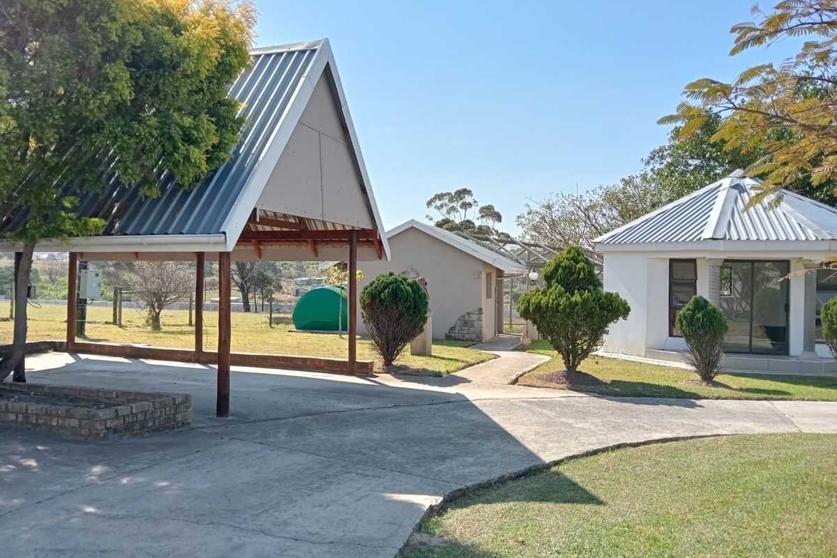 Exterior view of the farm property featuring a covered outdoor structure, paved pathways, and surrounding garden areas with established trees.