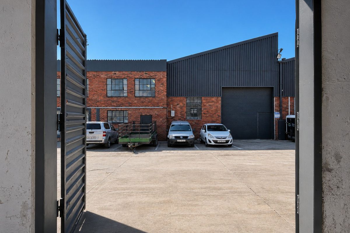 View of an industrial property exterior featuring a concrete yard, exposed brickwork, steel-framed windows, and a large roller shutter door.