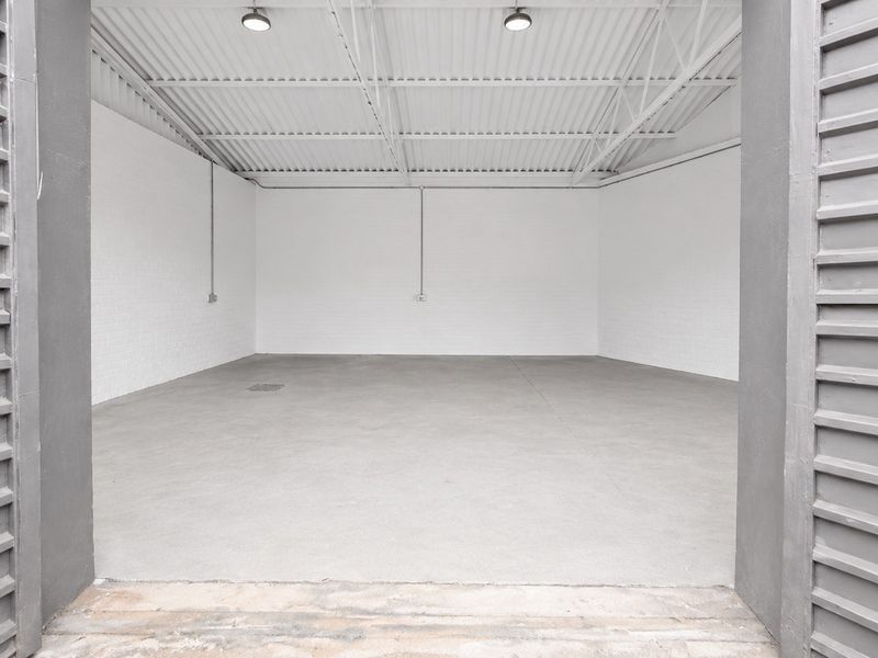 A clean, spacious industrial garage or warehouse unit featuring concrete flooring, exposed roof trusses, and bright white painted brick walls.