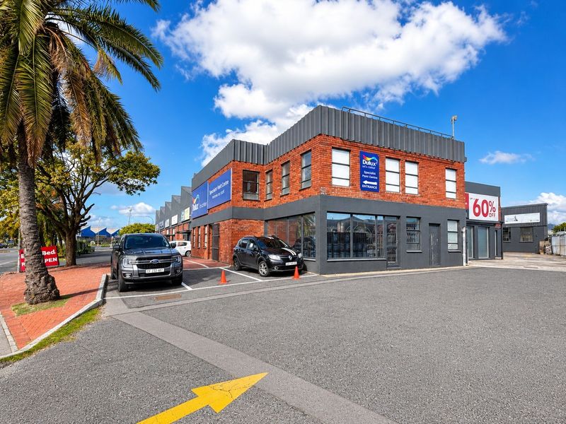 A well-maintained industrial commercial building featuring a brick facade, large display windows, and dedicated paved parking in a prominent street-facing location.