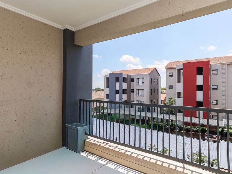 A clean, covered balcony featuring a metal balustrade and tiled flooring, offering an elevated view of the surrounding apartment complex.