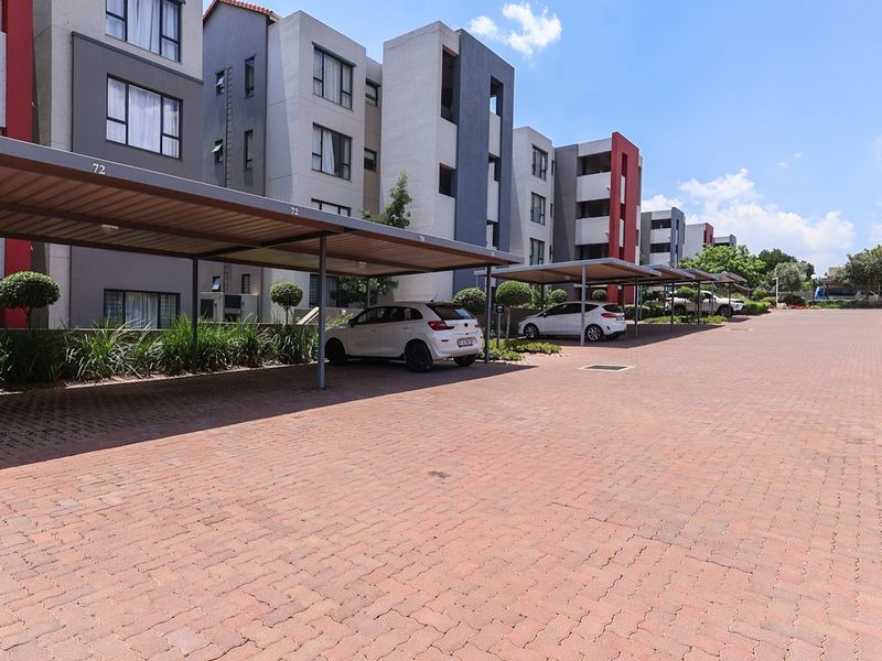 Exterior view of a modern apartment complex featuring covered parking bays and a well-maintained paved driveway area.