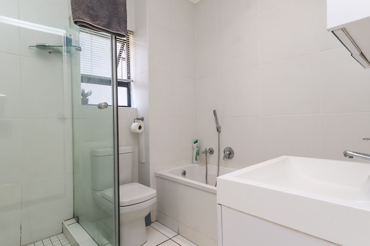 A clean, functional bathroom featuring a glass-enclosed shower, a built-in bathtub with a handheld mixer, and a modern wall-mounted basin.