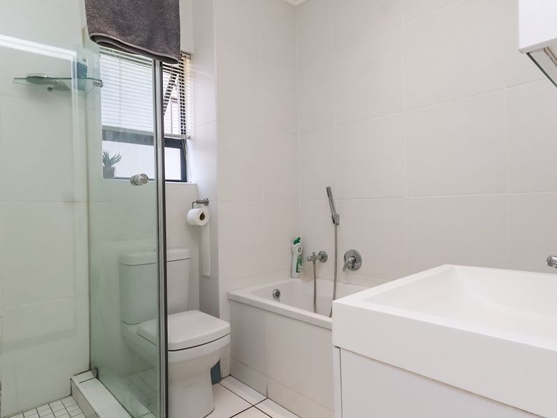 A clean, functional bathroom featuring a glass-enclosed shower, a built-in bathtub with a handheld mixer, and a modern wall-mounted basin.