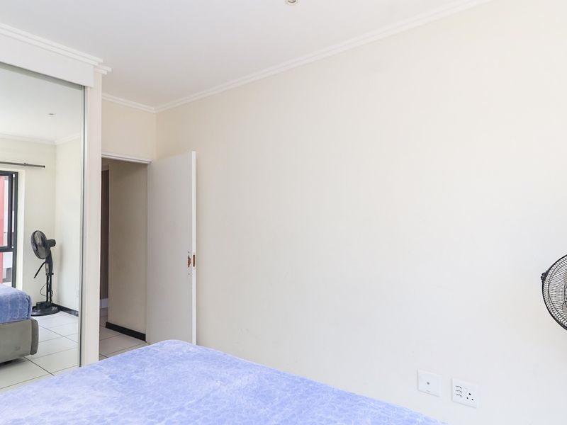 A bedroom featuring tiled flooring, a large mirrored sliding wardrobe, and neutral wall finishes, providing a functional and bright living space.