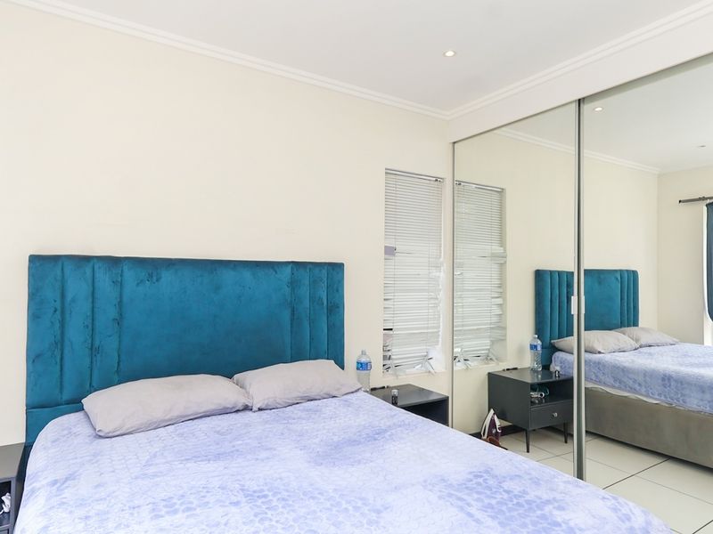 A well-maintained bedroom featuring tiled flooring, recessed downlighting, venetian blinds, and a large built-in mirrored wardrobe.