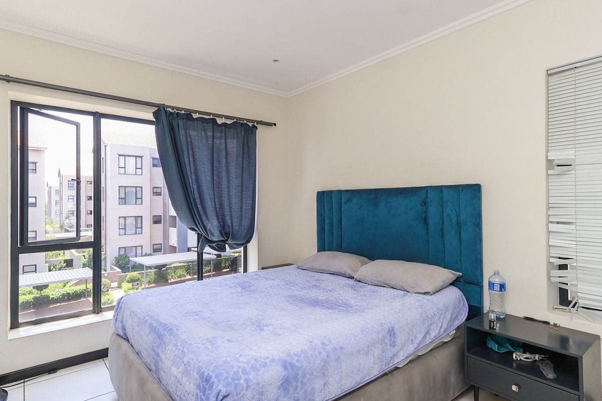 A bedroom featuring tiled flooring, aluminium window frames, and venetian blinds, offering natural light and a view of the surrounding apartment complex.