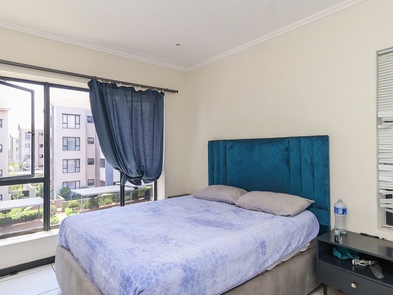 A bedroom featuring tiled flooring, aluminium window frames, and venetian blinds, offering natural light and a view of the surrounding apartment complex.