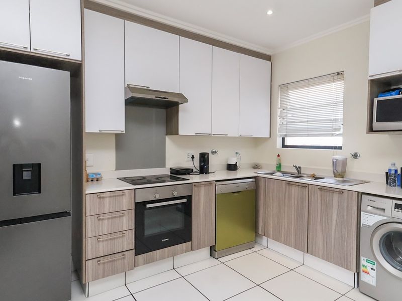 Modern kitchen featuring two-tone cabinetry, integrated appliances, electric hob, oven, extractor fan, and tiled flooring with ample storage space.