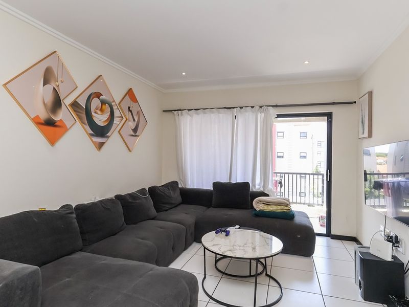 A bright and well-maintained living room featuring tiled flooring, recessed lighting, and direct access to a private balcony through a sliding glass door.